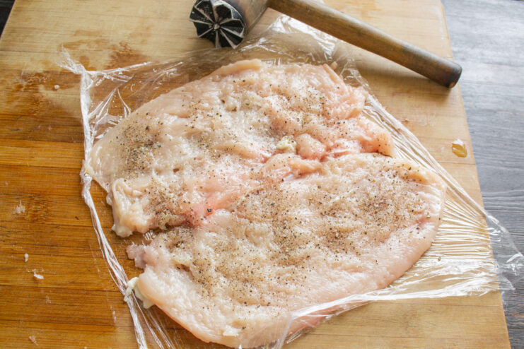 Seasoning the Chicken Breast Before Adding the Filling Pounded thin chicken breast being seasoned with salt and black pepper.