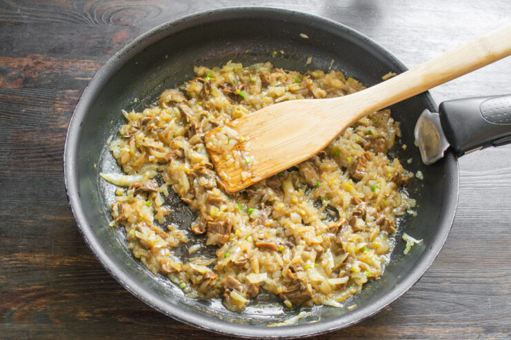 Sautéing Onions for the Savory Mushroom Filling Chopped onions being sautéed in a skillet with a wooden spatula.