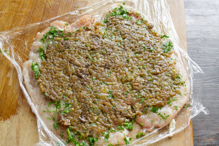 Spreading the Mushroom and Onion Filling on the Chicken A savory mushroom and onion filling being spread evenly over a pounded chicken breast.