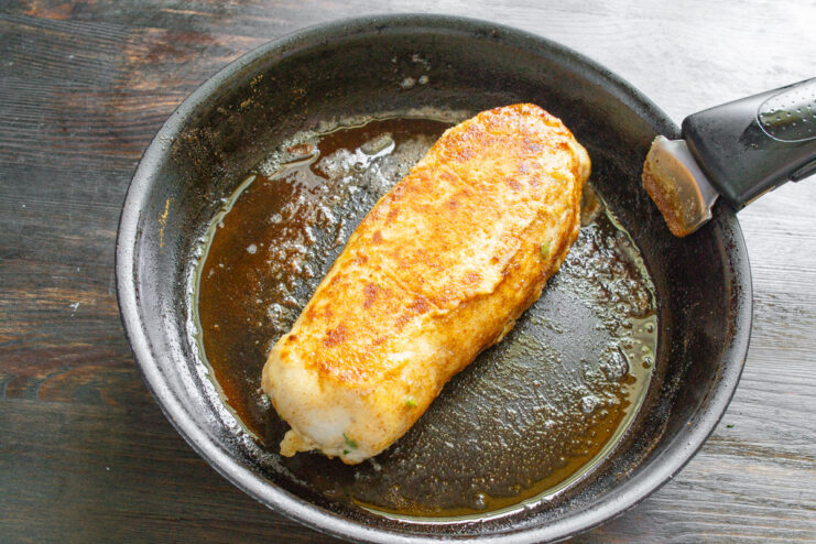 Searing the Chicken Roulade for a Golden-Brown Crust A breaded chicken roulade being pan-fried to a golden-brown color in a skillet.