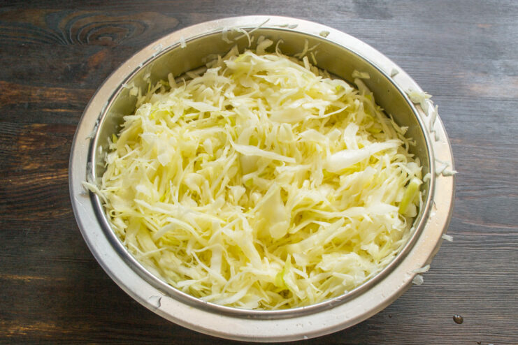 Massaging cabbage with salt to start the fermentation process Hands massaging shredded cabbage with salt in a bowl to release moisture.