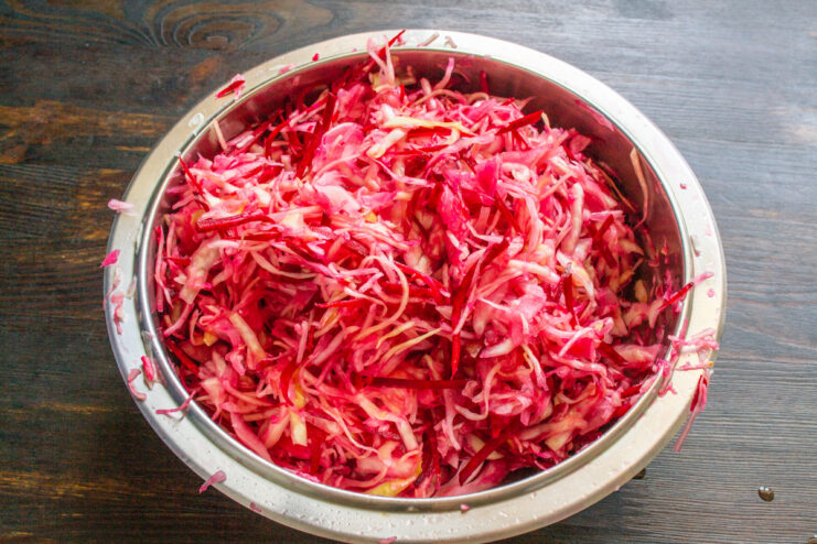 Combining all vegetables for the perfect fermented cabbage mix A bowl of shredded cabbage, beets, and horseradish being mixed by hand.