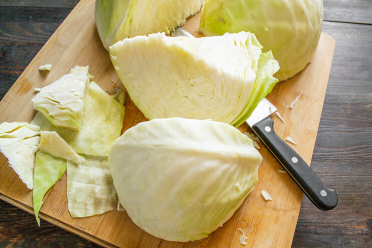 How to Prep Cabbage for Sauerkraut: Quartering and Coring A head of white cabbage cut into quarters with the core being removed.