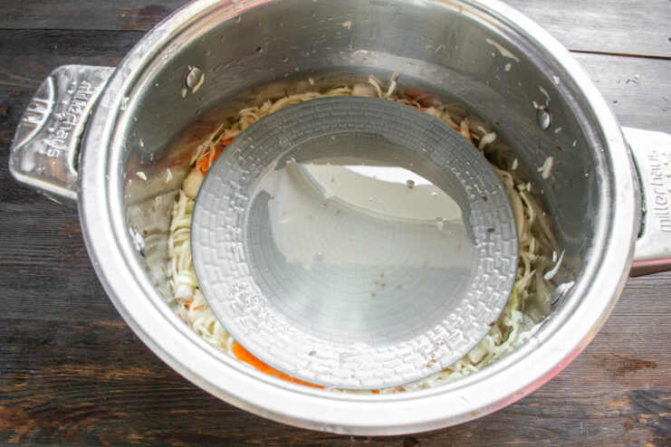 How to Properly Cover Your Sauerkraut for Fermentation A pot of cabbage for sauerkraut covered with a plate and a weight, ready for fermentation.
