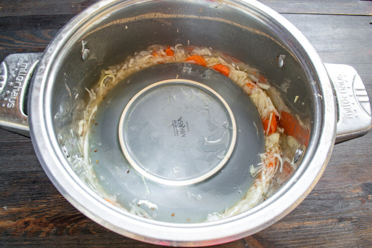Daily Maintenance: Stirring Your Fermenting Sauerkraut Stirring the fermenting cabbage in a pot to release gases.