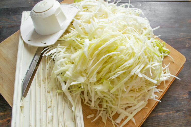 Shredding Cabbage for Perfectly Textured Sauerkraut Shredding white cabbage finely using a knife on a wooden cutting board.