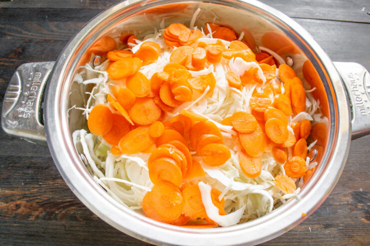 Adding Carrots to Sauerkraut for Color and Sweetness Thinly sliced carrot rounds being added to a pot of shredded cabbage.