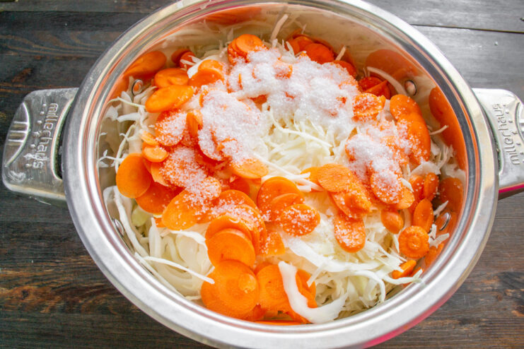 Seasoning the Cabbage and Carrots for Fermentation Sprinkling a salt and sugar mixture over shredded cabbage and carrots in a pot.