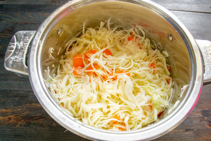 Massaging Cabbage to Release Brine for Fermentation Hands massaging shredded cabbage and carrots with salt and sugar in a pot.