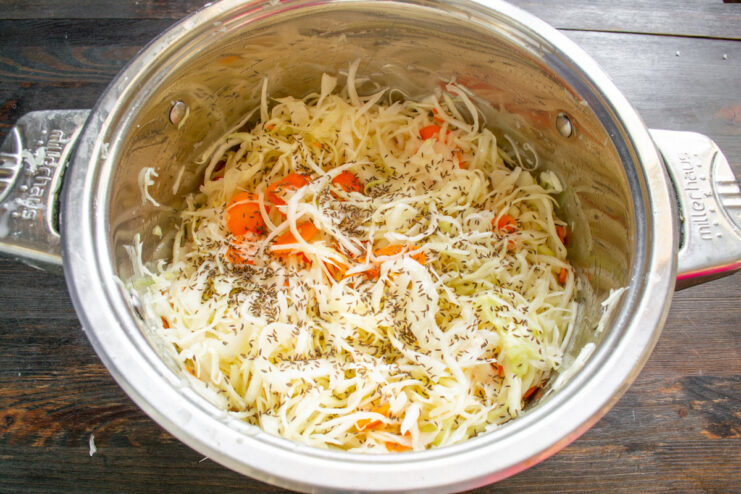Adding Aromatic Caraway Seeds for Classic Sauerkraut Flavor Adding caraway seeds to the mixture of cabbage and carrots in a pot.