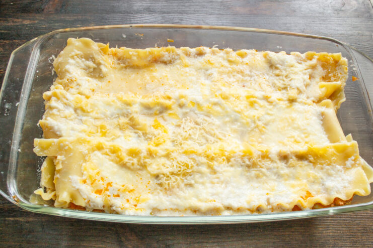 Topping the lasagna with a generous layer of cheese Sprinkling grated cheese over the top layer of the assembled lasagna.