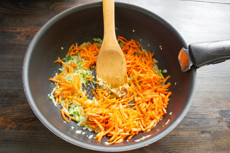 Adding grated carrot for sweetness and color Grated carrot being added to sautéed onions and celery in a skillet.