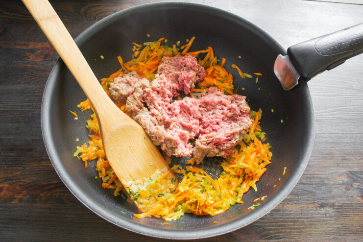 Browning the ground meat with vegetables Ground beef being added to the pan with sautéed carrots, onions, and celery.