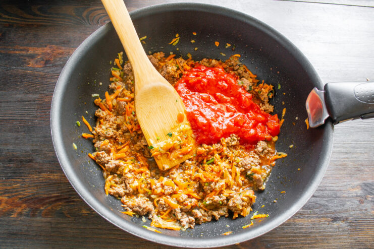 Adding canned tomatoes to the meat sauce Adding canned chopped tomatoes to the meat sauce in the skillet.