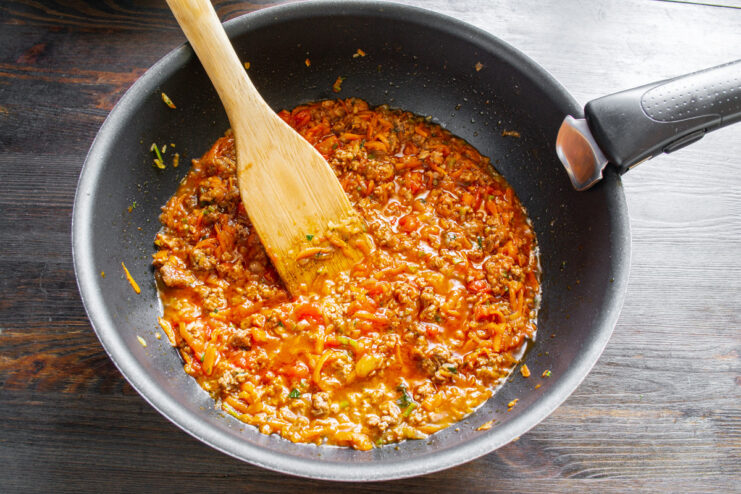 Simmering the sauce with broth for rich flavor Pouring broth into the Bolognese sauce simmering in a skillet.