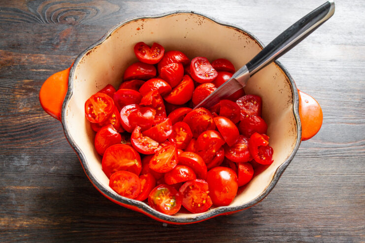 Preparing Tomatoes for the Lecho Sauce Base Fresh red tomatoes being cut into quarters on a cutting board.