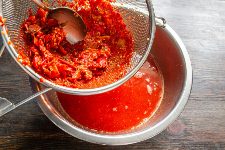 Straining the Sauce for a Smooth Lecho Texture Cooked tomatoes and physalis being pressed through a sieve to create a smooth vegetable puree.