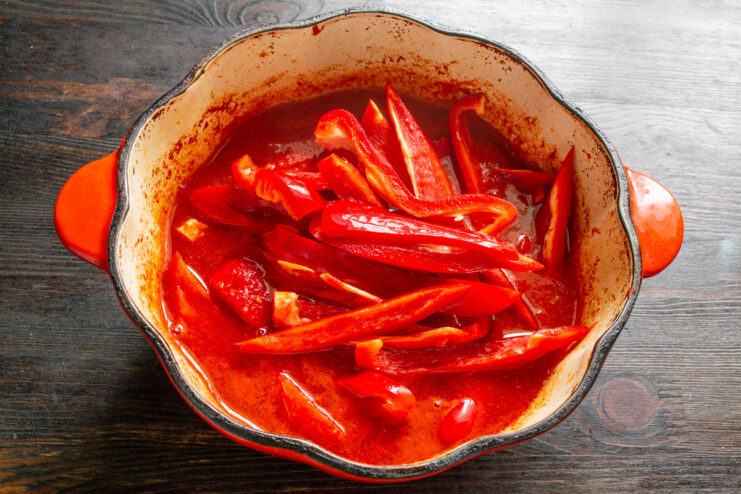 Slicing Red Bell Peppers for the Lecho Slicing a red bell pepper into thin strips on a cutting board.