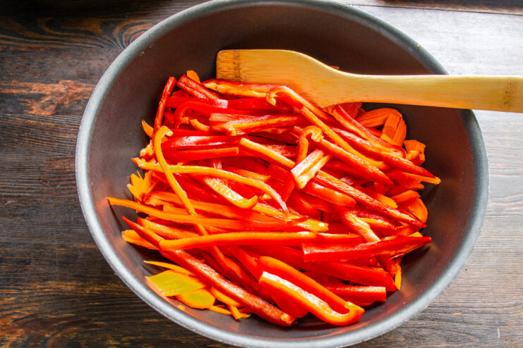 Combining Vegetables for the Stew A pot containing julienned carrots and sliced red bell peppers, the base for the lecho.