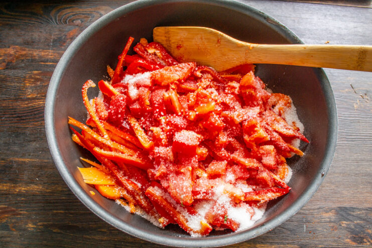 Seasoning the Lecho with Salt and Sugar Adding a spoonful of salt and sugar to the pot of chopped vegetables for lecho.