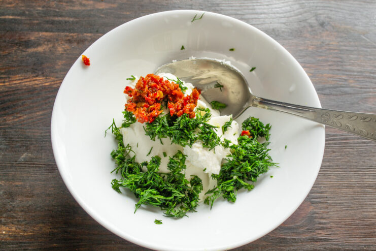 Adding Dill and Spicy Adjika to the Cheese Adding chopped dill and red adjika paste to a bowl of creamy curd cheese.