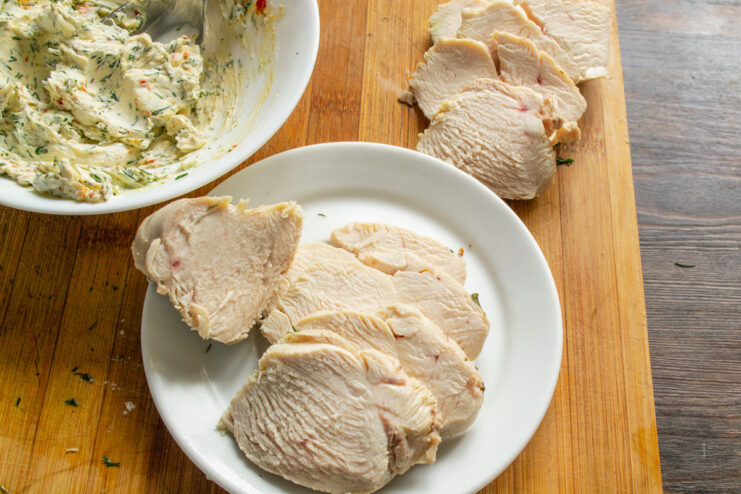 Slicing the Cooked Chicken Breast A hand slicing a cooked, skinless chicken breast into thin slices on a cutting board.