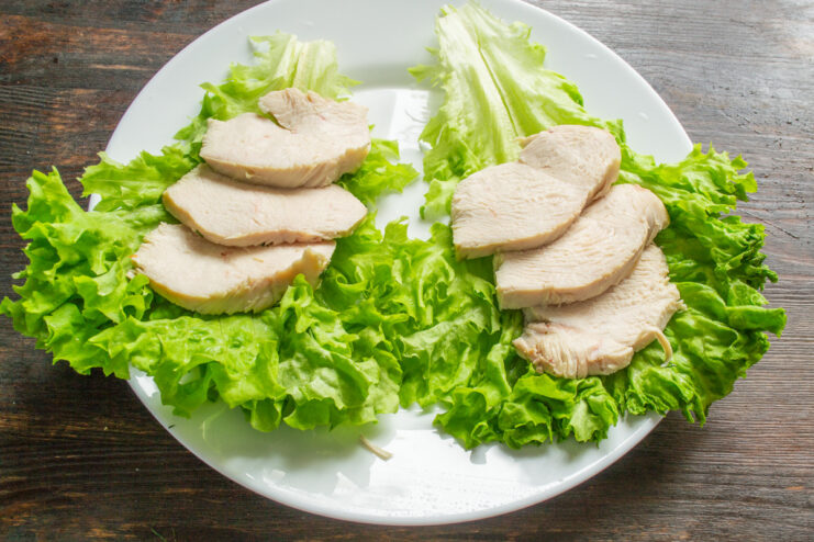 Arranging Chicken Slices on Lettuce Leaves Sliced chicken breast arranged on a bed of fresh lettuce leaves on a plate.