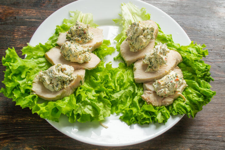 Topping the Chicken with Creamy Cheese Spread Spoonfuls of creamy cheese spread being placed on top of sliced chicken breast.