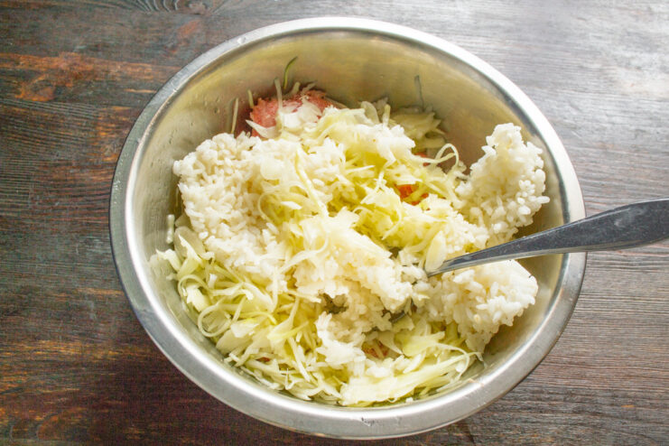 Combining Meat, Cabbage, and Rice for the Filling Adding cooked rice to a bowl with ground meat and shredded cabbage.