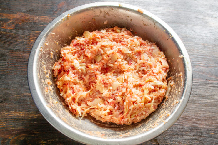 Mixing the Ingredients for Uniform Flavor and Texture Hands thoroughly mixing the ground meat, cabbage, rice, and spices in a bowl.