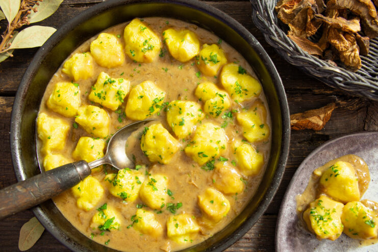 A white bowl filled with lazy potato varenyky smothered in a creamy mushroom sauce and garnished with fresh herbs.