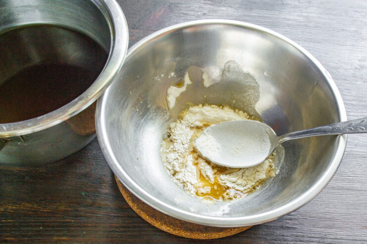 Creating a slurry with flour and broth to thicken the sauce. Whisking flour and a small amount of cold mushroom broth in a bowl to create a smooth paste.