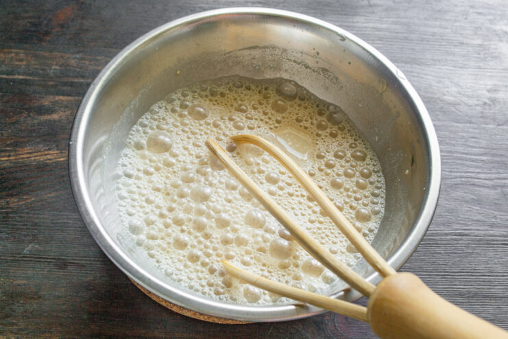Whisking the sauce to ensure it's smooth and lump-free. A hand whisking the mushroom sauce in a bowl until it reaches a smooth, consistent texture.