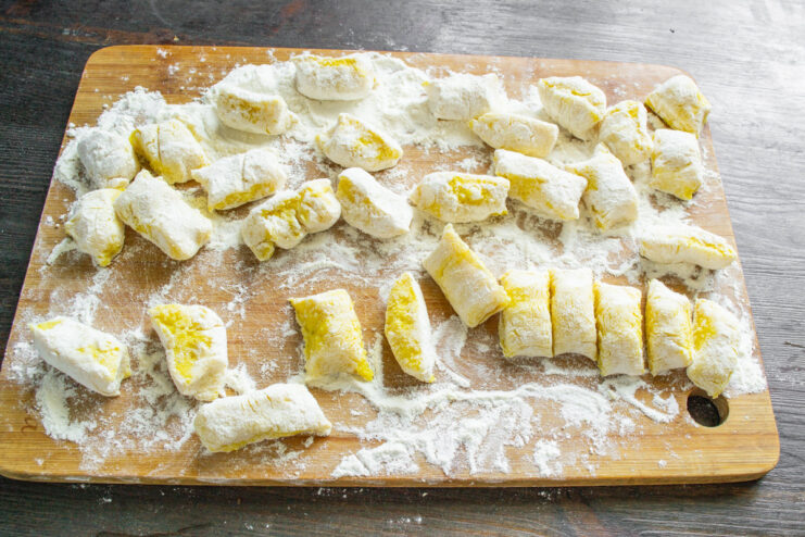 Cutting the dough logs into individual dumplings. Cutting a log of potato dough into small, gnocchi-like pieces on a floured surface.