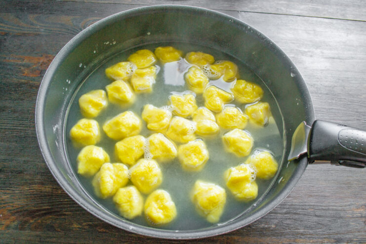 Boiling the lazy varenyky until they are cooked through. Lazy potato varenyky boiling in a pot of water, floating to the surface.