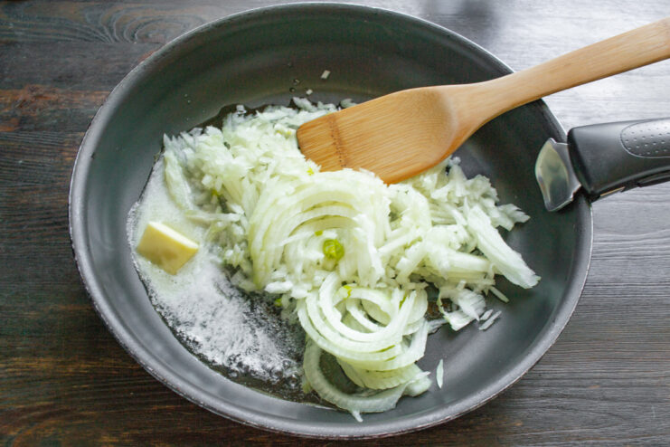 Sautéing onions until soft and translucent as a base for the sauce. Chopped onions being sautéed in a pan with butter until they become soft and translucent.