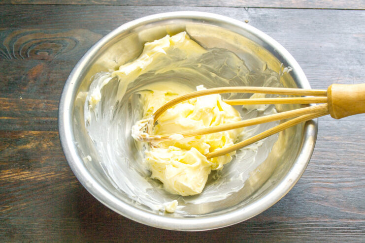 A glass bowl with softened butter being whisked.