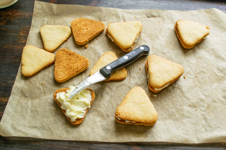Spreading a layer of lemon cream onto a baked cookie.