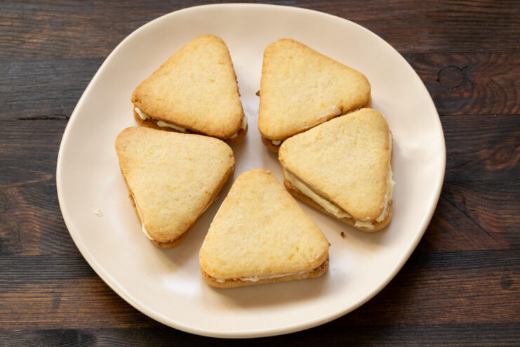 A stack of finished lemon cookies with lemon cream filling on a plate.