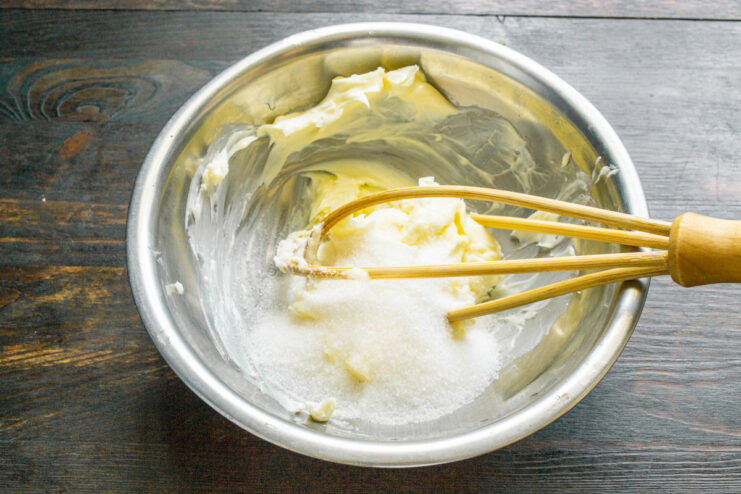 Adding sugar to a bowl of whipped butter.