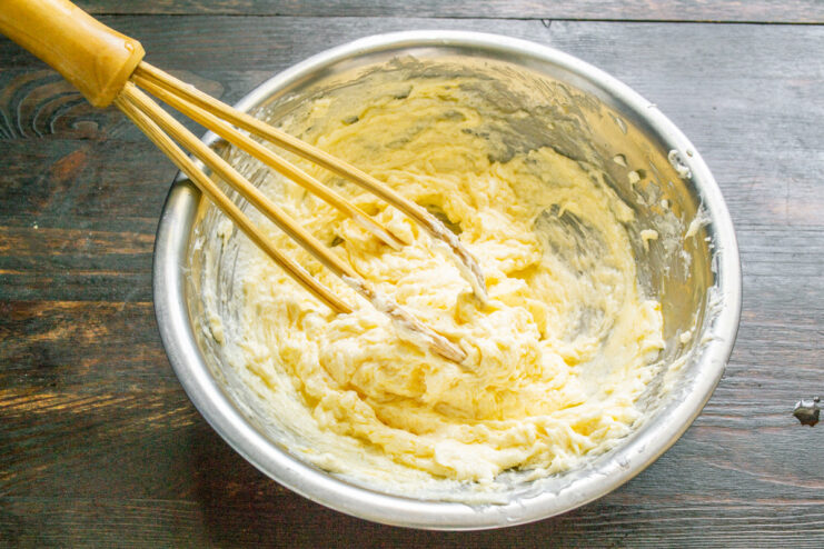 An egg is added to the creamed butter and sugar mixture in a glass bowl.