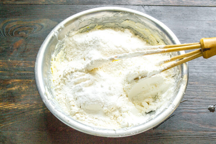 Adding flour mixture to the wet ingredients in a glass bowl to make cookie dough.