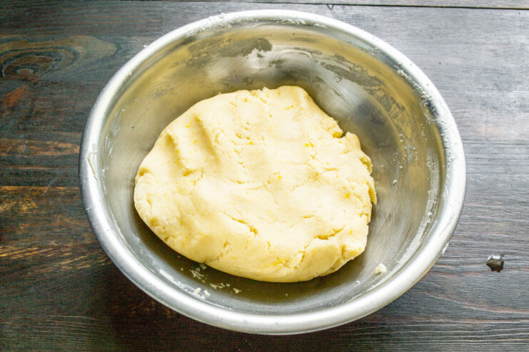A hand kneading the lemon cookie dough in a glass bowl.