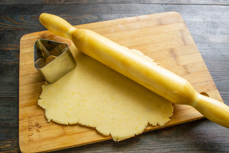 Rolling out the lemon cookie dough on a board with a rolling pin.