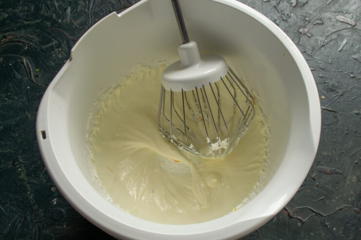 Preparing the Creamy Glaze Base A mixer whipping softened butter and powdered sugar in a bowl to create a fluffy base for the glaze.