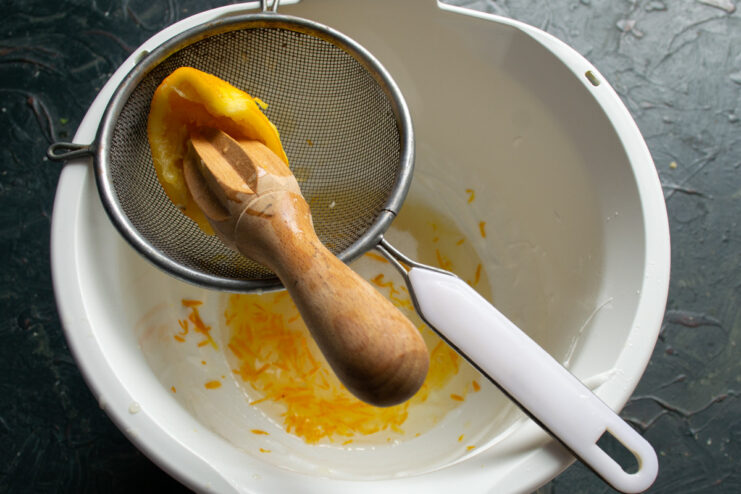 Adding Fresh Lemon Zest for Flavor A hand grating fresh lemon zest into a bowl with other ingredients for the bun dough.