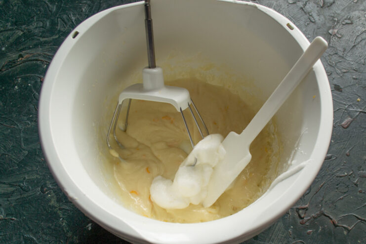 Folding in Whipped Egg Whites A spatula folding fluffy whipped egg whites into the smooth yellow batter in a bowl.