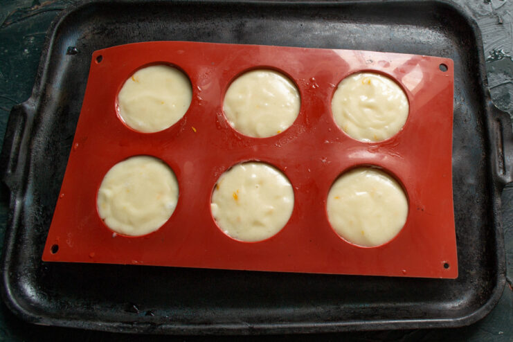 Portioning the Batter into Baking Molds A baking pan with individual molds being filled with the prepared lemon bun batter.