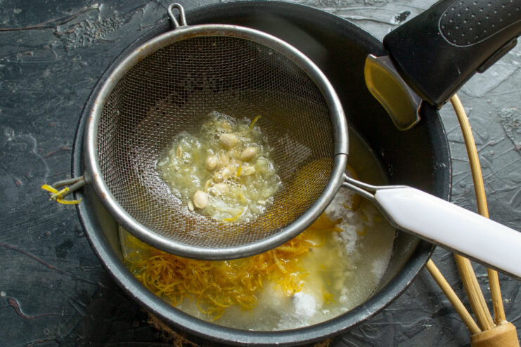 Straining Lemon Juice to Ensure a Smooth Curd Texture Straining fresh lemon juice through a fine-mesh sieve into the saucepan.