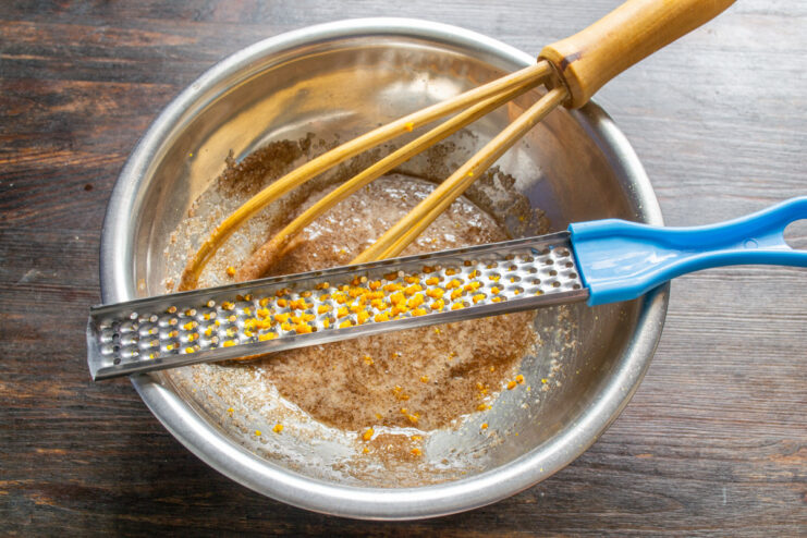 Step 2: Adding freshly grated orange zest for a citrusy aroma Grating fresh orange zest into a bowl with other muffin ingredients.